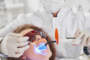 A young child smiling in a dental chair with a parent nearby and a dentist showing a toothbrush.