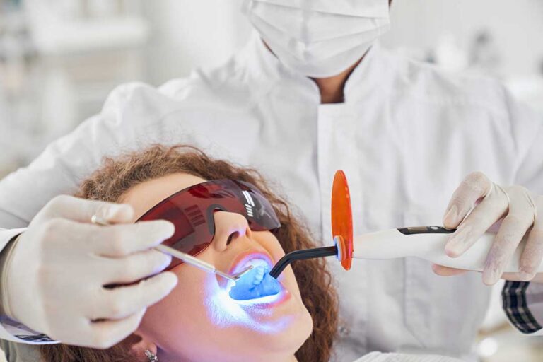 A young child smiling in a dental chair with a parent nearby and a dentist showing a toothbrush.