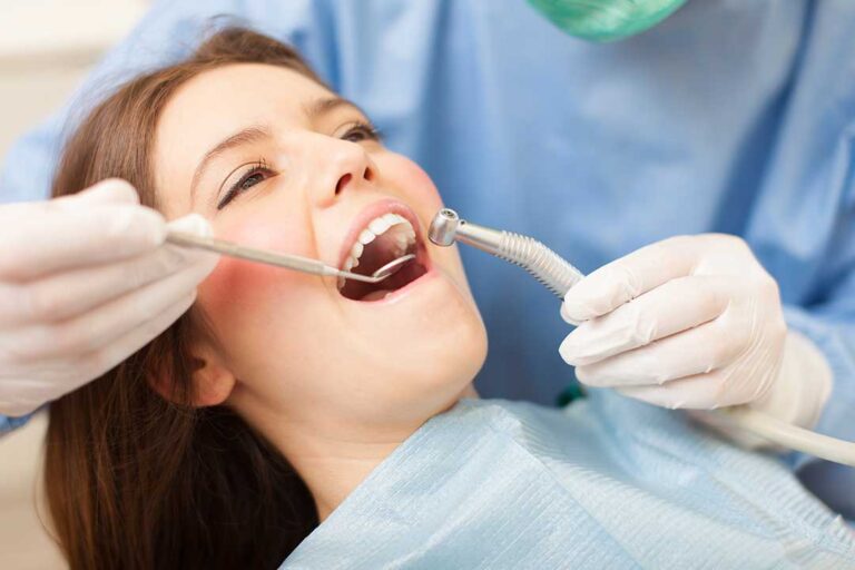 Person gently brushing teeth with a soft toothbrush beside a glass of water and dental floss.